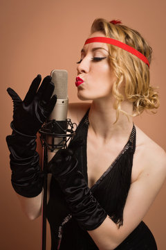 Pretty actress in black retro dress singing with microphone