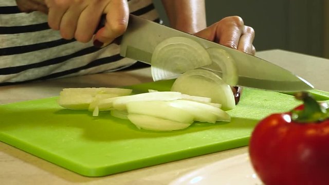 Cooking ratatouille. Female hands cutting onion into slices on plastic cutting board. HD
