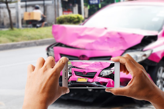 Close up hand holding smartphone and view photo of pink car accident