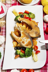 Two fried carp steaks served on a white plate with boiled potatoes and broccoli.