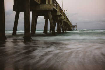 Froth ocean waves slowly climbing sea bed underneath the strong isolated pier dock