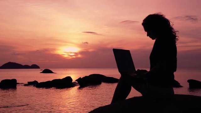 silhouette of girl working with laptop at sunset on the sea