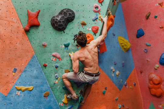 Muscular and fit topless man exercise bouldering and climbing indoor at artificial wall
