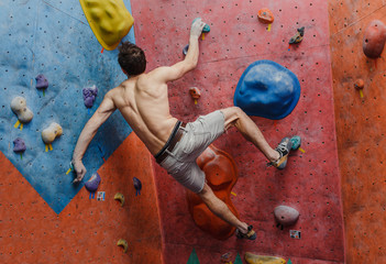 Muscular and fit topless man exercise bouldering and climbing indoor at artificial wall