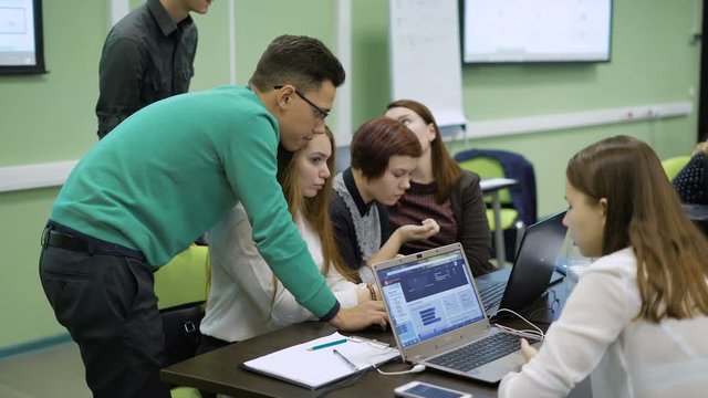Smart man helping a group of girl students in computer lab.