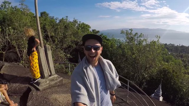 Happy young bearded man making GoPro selfie at the poplular viewpoint at Koh Phangan, Thailand.
