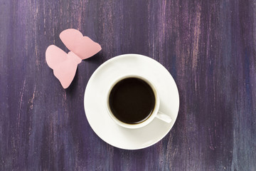 Black coffee and paper butterfly on purple background