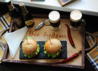 Burgers on a wooden tray. Beer glasses on served table. The atmosphere is fun. For two