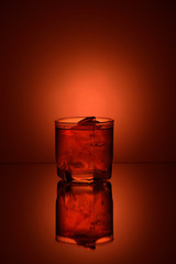 glass of whiskey with ice on orange background with a mirror image