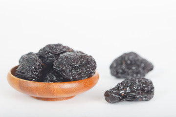 Dried plums or prunes in wooden bowl over white background