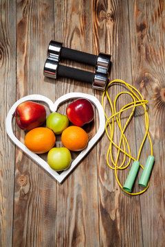 White heart, apples and oranges, healthy diet, dumbbells  a jump rope on  wooden background