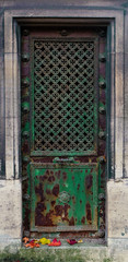 Rusty old green iron door - the metal is decaying and rusting. In the middle is a repeating cross pattern with small clover (quatrefoil) ornaments. The doorframe is rectangle.