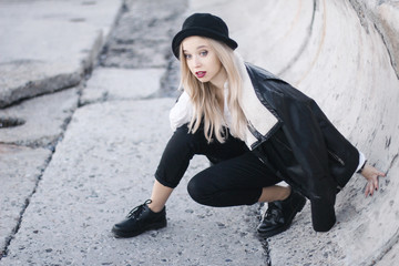 girl in black coats, trousers and a cap is pushed away from the wall. blonde with a surprise on his...