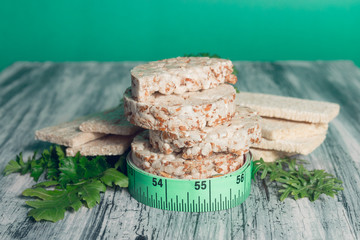 Pieces of crispbread near measuring tape and green arugula on grey background. Diet concept. Healthy food.