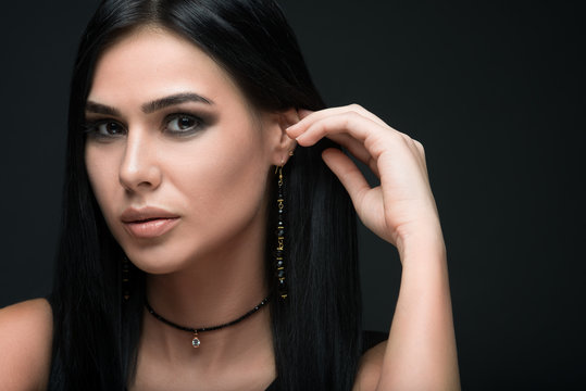 Beauty shot of brunette luxury model in dark dress and jewelry on dark background