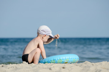 Little blonde boy playing with sand on the seashore