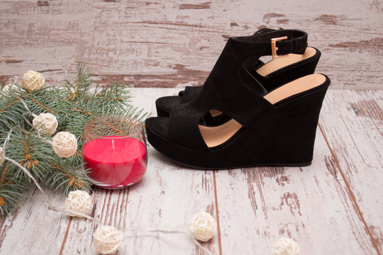 Black suede shoes on a wooden background, fir branch wreath and candle. fashion concept