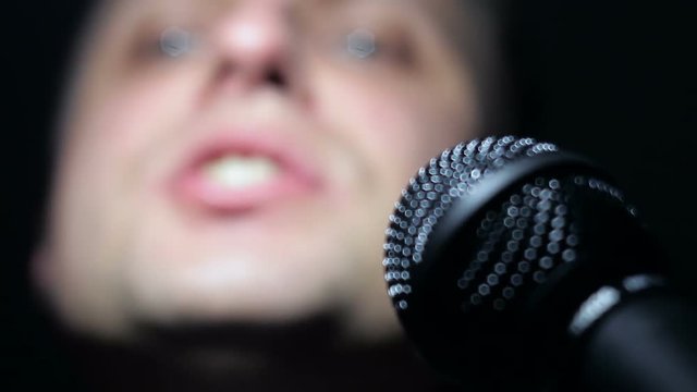 Close-up of man singing to microphone in dark