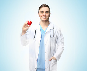 Young doctor with red heart on light blue background