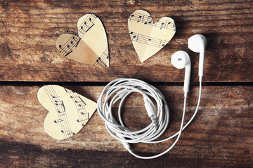 Paper hearts with music notes and earphones on wooden background