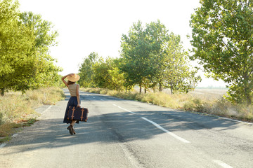 Young woman with suitcase walking along road