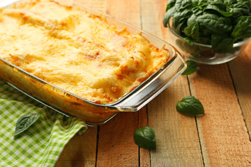 Traditional lasagna in glass baking dish and napkin on wooden table