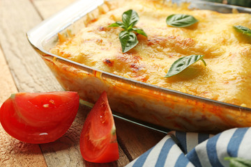 Traditional lasagna in glass baking dish and tomatoes on wooden table