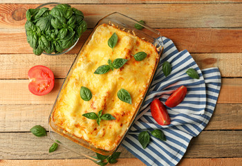 Traditional lasagna in glass baking dish and tomatoes on wooden table
