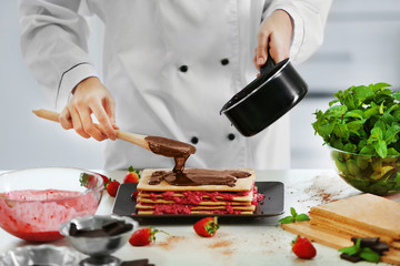 Cooking concept. Professional confectioner decorating delicious cake with chocolate frosting, closeup