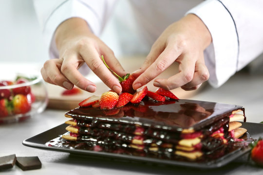 Cooking concept. Professional confectioner decorating delicious cake with strawberry, closeup