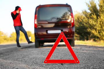 Red warning triangle on asphalt road. Driver near broken down car
