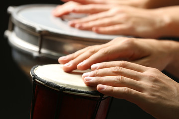 Hands of man playing African drum on dark background, close up