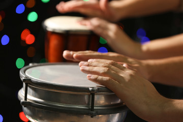 Hands of man playing African drum against defocused lights