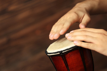 Hands of man playing African drum on brown blurred background, close up
