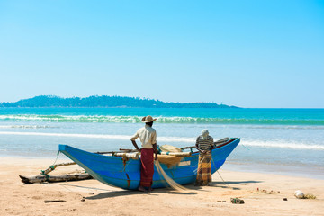 Fototapeta premium Two fishermen reviewing the fish net near traditional Sri Lanka's boat on ocean shore
