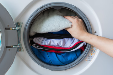 hand and puts the laundry into the washing machine