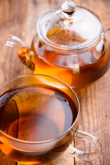 Tea in glass teapot and cup on wooden table still life, shallow focus on cup