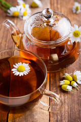 Herbal chamomile tea in cup and glass teapot with fresh chamomile herbs on vintage wooden table background