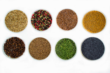 Herbs and seasonings - dried coriander, peppercorn, flax seeds, mustard, clove, cumin, parsley and poppy seeds in a transparent dish isolated on white background.