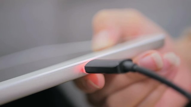 Woman's hand plugging black lightning charging cable into pc digital tablet - USB data cable connecting on modern gadget. Close up shot