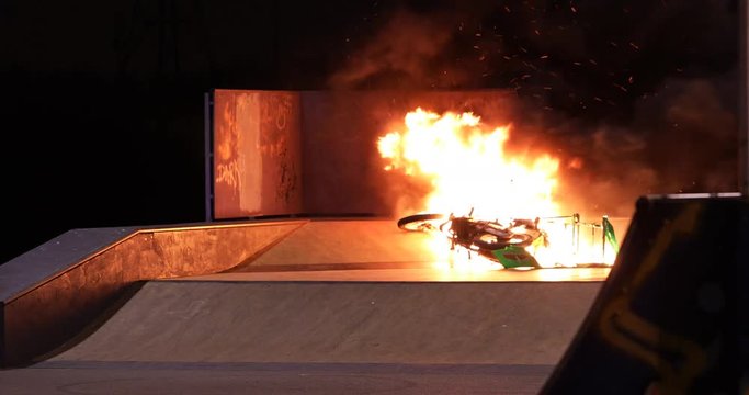4K A scooter lays in a skate park at night, blazing with fire