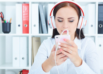 Beautiful girl  in headphones listening to music from smartphone in office.