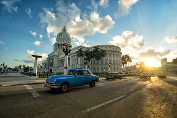 Poster Blauwe retro auto rijdt in de buurt van het oude koloniale Capitool in het centrum van Havana bij zonsondergang © simonovstas