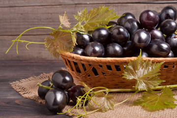 Blue grapes in a wicker basket on wooden table