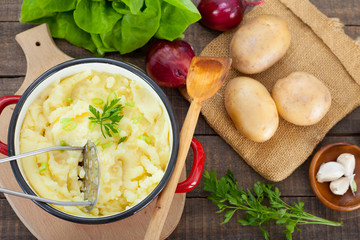 Homemade  mashed potato with parsley in the pot. Fresh potatoes, onion, garlic and lettuce on rustic table.