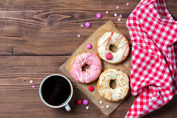 Donuts with sprinkles hearts, smarties and cup of coffee, wooden background, top view