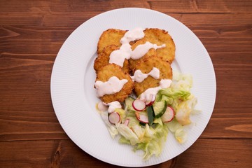 Vegetarian healthy dish consist from cauliflower pancakes and fresh vegetable green salad with tin slices of radish. On the top of dish is a topping or dip from yogurt and chili.