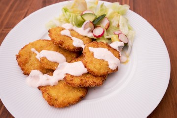 Vegetarian healthy dish consist from cauliflower pancakes and fresh vegetable green salad with tin slices of radish. On the top of dish is a topping or dip from yogurt and chili.