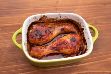 Chicken drumsticks marinated in soya sauce, honey, beer and tomatoes and than roasted in small ceramic roasting pan. Close up Picture served in the pan without any side dish or salad. 