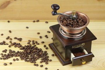 Old-style manual coffee grinder on a rustic table with wooden planks. Around the mill are scattered...